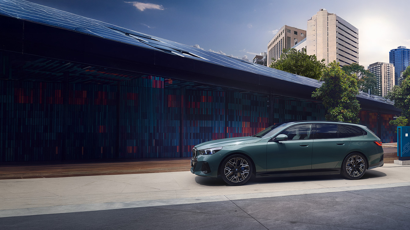 BMW i5 Touring in Seitenansicht an einer Ladestation vor moderner Stadtkulisse