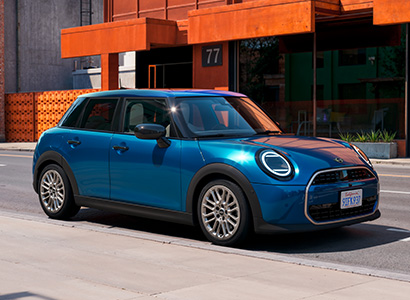 Blaues Mini Cooper 5-Türer fährt auf einer städtischen Straße.