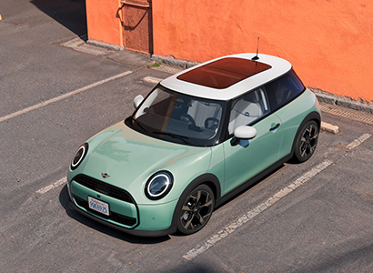Mintgrüner Mini Cooper im Seitenprofil vor orangenen Gebäude.