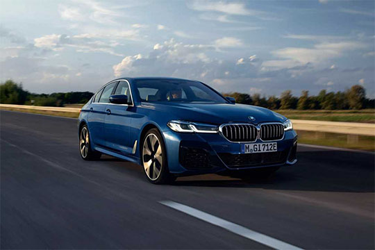 Dunkelblauer BMW fährt dynamisch auf einer Straße mit bewölktem Himmel.