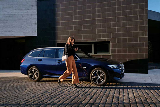 Frau geht neben einem dunkelblauen BMW Kombi auf einem gepflasterten Weg.