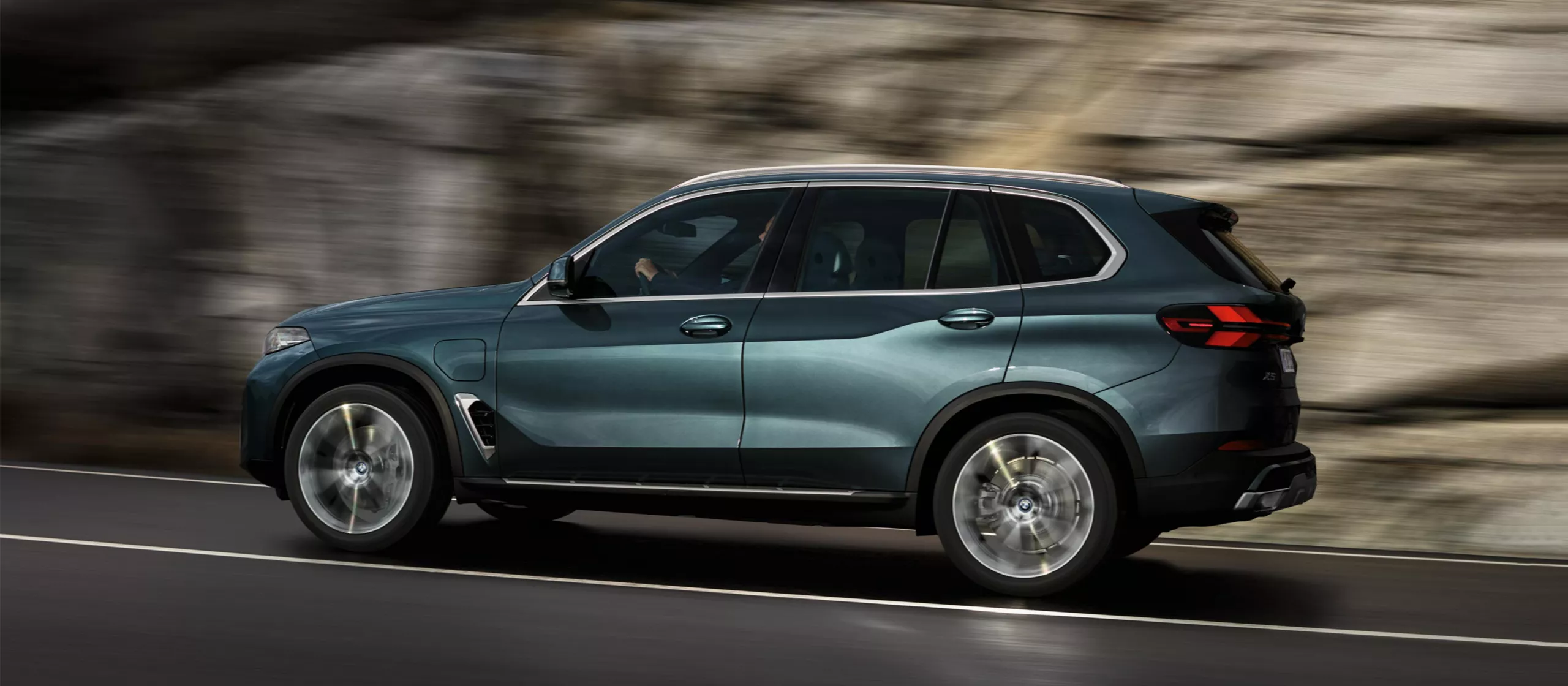 BMW Müller PREMIUM SELECTION GARANTIE Dunkelblauer BMW X5 SUV fährt auf einer Straße mit Felswand im Hintergrund