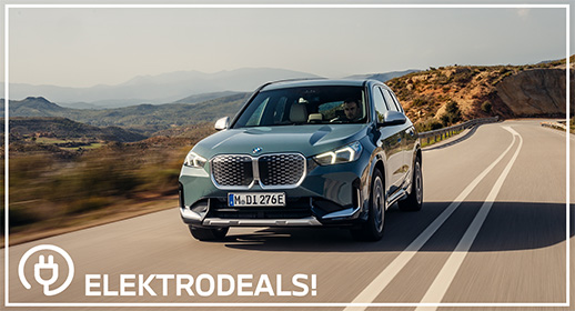 Vorderansicht eines grauen BMW iX1 Elektro-SUVs mit Kennzeichen 'MDI 276E', der auf einer kurvigen Landstraße fährt. Mit 'Elektrodeals!'-Logo."