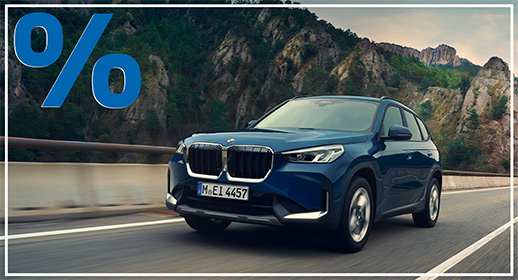 Blauer BMW X1 SUV in Fahrt vor einer imposanten Felskulisse; blaues Prozent-Symbol oben links.