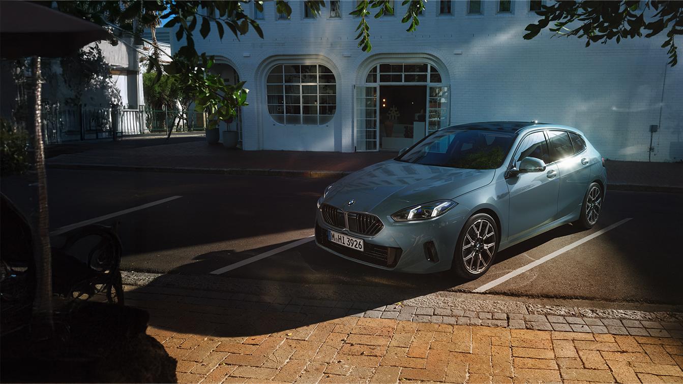 Hellblauer BMW 1er in Front-Seitenansicht, geparkt an einer Straße vor einem weißen Gebäude