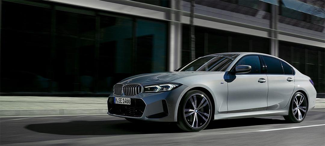 BMW 318i Limousine Angebot Hellgraue BMW 318i Limousine in Bewegung auf einer Straße vor einem modernen Gebäude, unscharfer Hintergrund deutet auf Geschwindigkeit hin. Das Bild zeigt das spezifische Modell des Angebots dynamisch