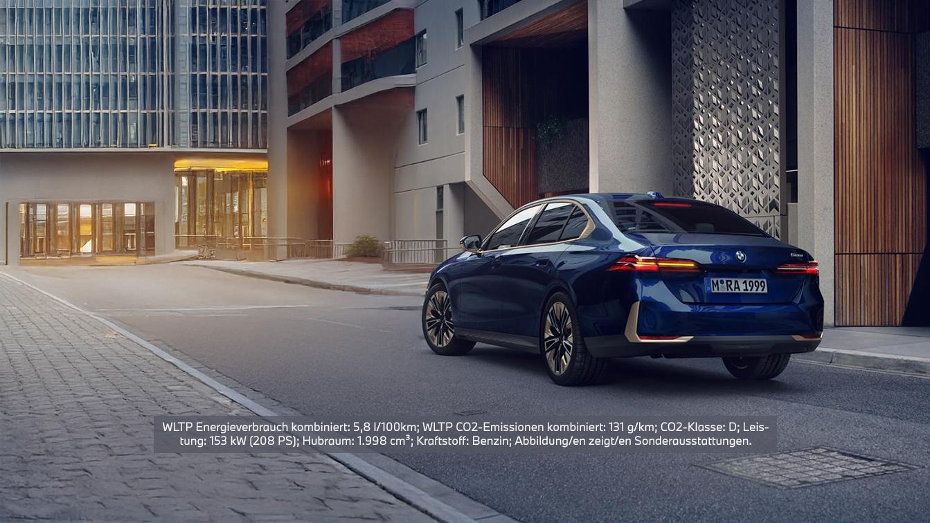 Eine dunkelblaue BMW 520i Limousine ist von hinten rechts auf einer Straße vor modernen Gebäuden geparkt. Das Fahrzeug hat ein Kennzeichen mit der Aufschrift "M RA 1999" und zeigt die Rückleuchten sowie leichte Chromakzente. Im unteren Bereich des Bildes befindet sich eine Texteinblendung mit folgenden technischen Daten: "WLTP Energieverbrauch kombiniert: 5,8 l/100km; WLTP CO2-Emissionen kombiniert: 131 g/km; CO2-Klasse: D; Leistung: 153 KW (208 PS); Hubraum: 1.998 cm³; Kraftstoff: Benzin; Abbildung/en zeigt/en Sonderausstattungen."