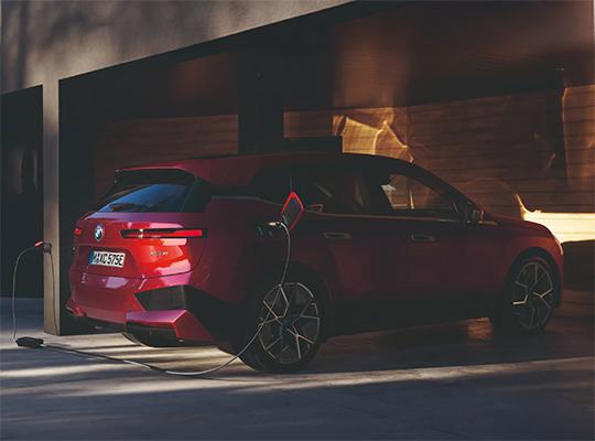 Ein rotes BMW iX Elektroauto ist rückwärts in einer Garage geparkt und an eine Ladestation angeschlossen.