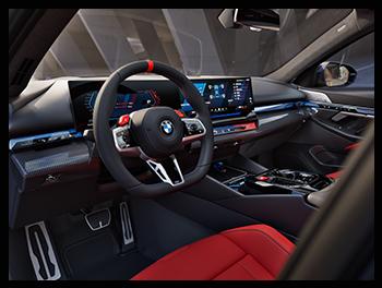 Das Cockpit der BMW M5 Limousine kombiniert Luxus mit Motorsport, erkennbar am unten abgeflachten M-Lederlenkrad mit roten M-Tasten, dem BMW Curved Display und der hochwertigen Ambientebeleuchtung.