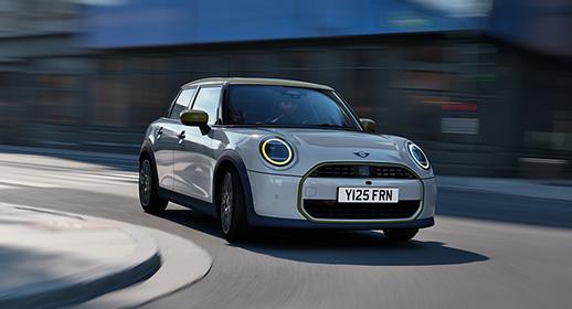Der MINI 5-Türer der exklusiven MINI x Paul Smith Edition in hellem Graublau während einer dynamischen Fahrt durch eine urbane Straße.