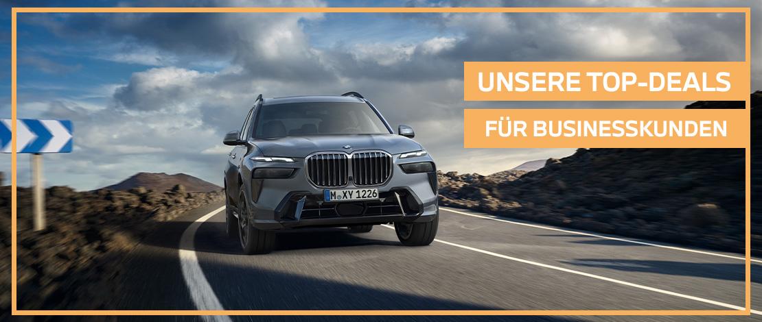Das Bild zeigt einen grauen BMW X7, der auf einer Straße fährt. Auf der rechten Seite des Bildes steht in großen Buchstaben „UNSERE TOP-DEALS FÜR GEWERBEKUNDEN“. Das gesamte Bild hat einen orangefarbenen Rahmen.