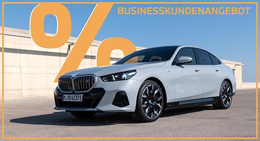 Das Bild zeigt eine hellgraue BMW i5 Limousine auf einer gepflasterten Fläche. Im oberen Teil steht der Text „GEWERBEKUNDENANGEBOT“, und links ist ein großes, oranges Prozentsymbol zu sehen. Ein orangefarbener Rahmen umgibt das gesamte Bild.