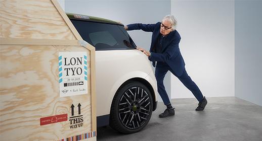 Designer Sir Paul Smith schiebt den neuen MINI Cooper der Paul Smith Edition aus einer hölzernen Transportkiste mit der Aufschrift „LON TYO“ heraus.