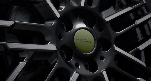 Detailaufnahme der schwarzen Leichtmetallfelge einer MINI Paul Smith Edition mit einer markanten, olivgrünen Nabendeckel-Abdeckung inklusive Paul Smith Signatur.