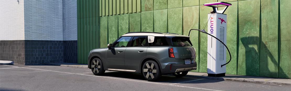 In diesen Aufnahmen wird der MINI Countryman SE ALL4 in seiner natürlichen Umgebung als modernes Elektro-SUV präsentiert. Das Fahrzeug besticht durch seine markante zweifarbige Lackierung, bei der ein tiefes Grün auf ein cremeweißes Dach trifft. Technisch ist das Modell auf Effizienz ausgelegt: Mit einer DC-Ladeleistung von bis zu 130 kW kann die Batterie in nur etwa 29 bis 30 Minuten von 10 % auf 80 % geladen werden. Im Alltag bietet der Wagen eine rein elektrische Reichweite von 399 bis 432 Kilometern nach WLTP-Standard.  Ein besonderes Augenmerk liegt auf dem Komfort beim Laden, etwa durch die Funktion Plug & Charge, die eine automatische Authentifizierung an der Ladesäule ermöglicht. Das Bild an der IONITY-Station verdeutlicht die Anbindung an eines der leistungsstärksten Ladenetzwerke Europas, das mit über 700 Standorten vor allem Langstreckenfahrten unterstützt. Die dortigen High-Power-Charging-Säulen liefern bis zu 350 kW (oder teilweise mehr) und nutzen dabei ausschließlich Strom aus erneuerbaren Energien. Über Programme wie MINI Charging erhalten Fahrer zudem Zugang zu attraktiven Tarifen und einer unkomplizierten Abrechnung im gesamten Netzwerk.