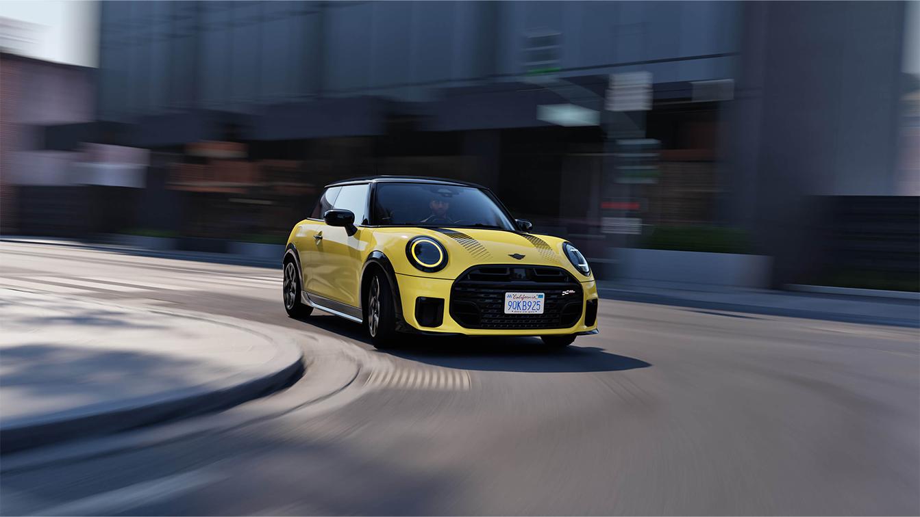 MINI Cooper Deals 2025 BMW Rhein Ein gelber Mini Cooper mit schwarzem Dach und sportlichen Details fährt mit leichtem Bewegungsunschärfe-Effekt auf einer städtischen Straße. Das Auto ist dynamisch in einer Kurve abgebildet, was die Geschwindigkeit betont. Im Hintergrund sind unscharf Gebäude und ein grauer Himmel zu sehen. Das Fahrzeug trägt ein US-amerikanisches Nummernschild aus Kalifornien.