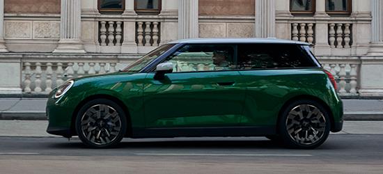 Ein grüner MINI 3-Türer mit weißem Dach fährt vor einer klassischen, historischen Fassade mit Säulen und Balustraden entlang.