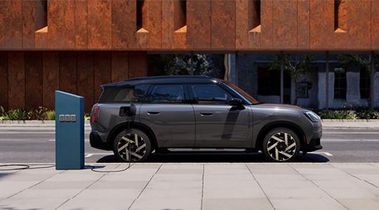 Das elfte Bild zeigt den MINI Countryman Electric beim öffentlichen Laden an einer Gleichstrom-Schnellladestation (DC) in einer städtischen Umgebung. Dank einer beeindruckenden Ladeleistung von bis zu 130 kW lässt sich die 64,6 kWh große Batterie in nur etwa 29 Minuten von 10 auf 80 Prozent aufladen, was das Fahrzeug absolut langstreckentauglich macht. Nutzer profitieren dabei von einem einfachen Zugang zu über 200.000 Ladepunkten europaweit via MINI Charging Card oder App, wobei die intelligente Plug & Charge-Funktion bei kompatiblen Säulen sogar einen vollautomatischen Start des Ladevorgangs ohne zusätzliche Authentifizierung ermöglicht. Dieses effiziente Zusammenspiel aus hoher Reichweite von bis zu 462 km und schnellen Ladezyklen unterstreicht die Vielseitigkeit des vollelektrischen SUV für Alltag und Reisen.