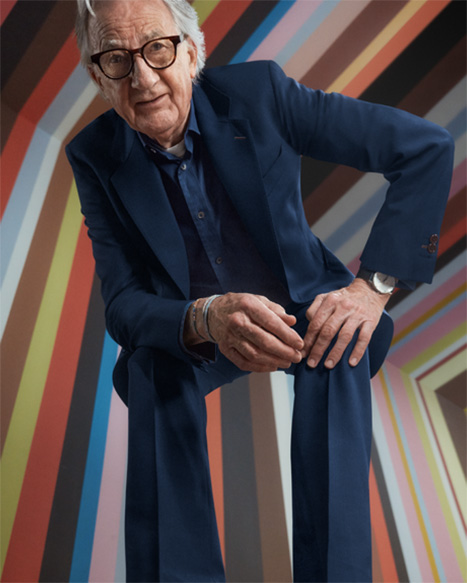 Modedesigner Sir Paul Smith im blauen Anzug posiert vor einem dynamischen Hintergrund im ikonischen, bunten Paul Smith Streifendesign der MINI Kollaboration.